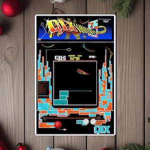 May include: A QIX arcade game sticker featuring a retro design with orange, blue, and black colors. The sticker has the game's title at the bottom and a detailed game screen. The sticker is placed on a wooden surface with Christmas decorations.