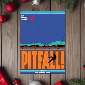 May include: A rectangular sign featuring the Pitfall! video game cover art. The design includes a blue sky, orange text, and a silhouetted figure swinging on a vine. The text reads "Pitfall!" and "Activision for the Atari 5200."