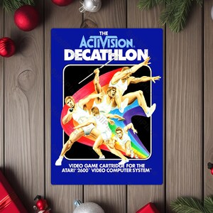 May include: A blue video game cartridge for the Atari 2600 featuring the title "The Activision Decathlon." The cover art depicts athletes in various track and field events, with a rainbow arch and the game's title in white.