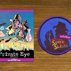 May include: A vintage Atari 2600 game cartridge for Private Eye, a detective game by Activision. The game cartridge features a cartoon detective with a magnifying glass and a cityscape in the background. The cartridge is purple and has the Activision logo and the game title.