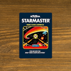 May include: A vintage Atari Starmaster video game cartridge. The cartridge has a dark blue background with the game title in white and a colorful space-themed graphic. The text "ACTIVISION" and "VIDEO GAME CARTRIDGE" are also visible.
