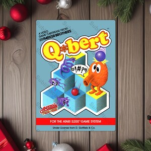 May include: A retro video game cartridge for the Atari 5200 game system featuring the game Q*bert. The cartridge has a light blue background with the game's title in yellow and orange, and a cartoon character. The game's logo and characters are prominently displayed.