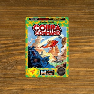 May include: A retro video game cartridge for the Nintendo Entertainment System. The label features the game title "Cobra Command" with a vibrant action scene of a helicopter and military vehicles. The Data East logo is visible.