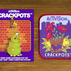 May include: Two vintage Activision "Crackpots" items. One is a video game cartridge with a purple background, brick wall, and a cartoon caterpillar. The other is a patch with a purple background, flowers, and a cityscape.