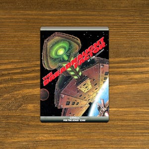 May include: A vintage Atari 5200 game cartridge titled "The Dreadnaught Factor" by Tom Loughry. The cover art features a space scene with a large, detailed spaceship and the game's title in red. The cartridge is set against a wooden background.