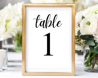 May include: Gold-framed table number card with the word "table" in cursive script and the number "1" in a bold, black font.