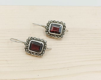 May include: A pair of silver earrings with a square-shaped red gemstone set in a silver frame with a marcasite border.