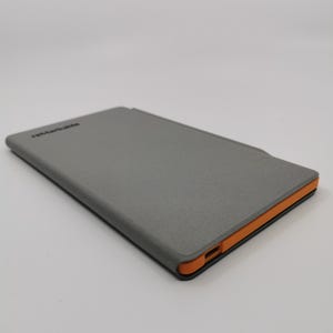 May include: A gray tablet case with an orange border. The case has a textured surface and the word "reMarkable" printed on the top. The case is rectangular and appears to be closed.