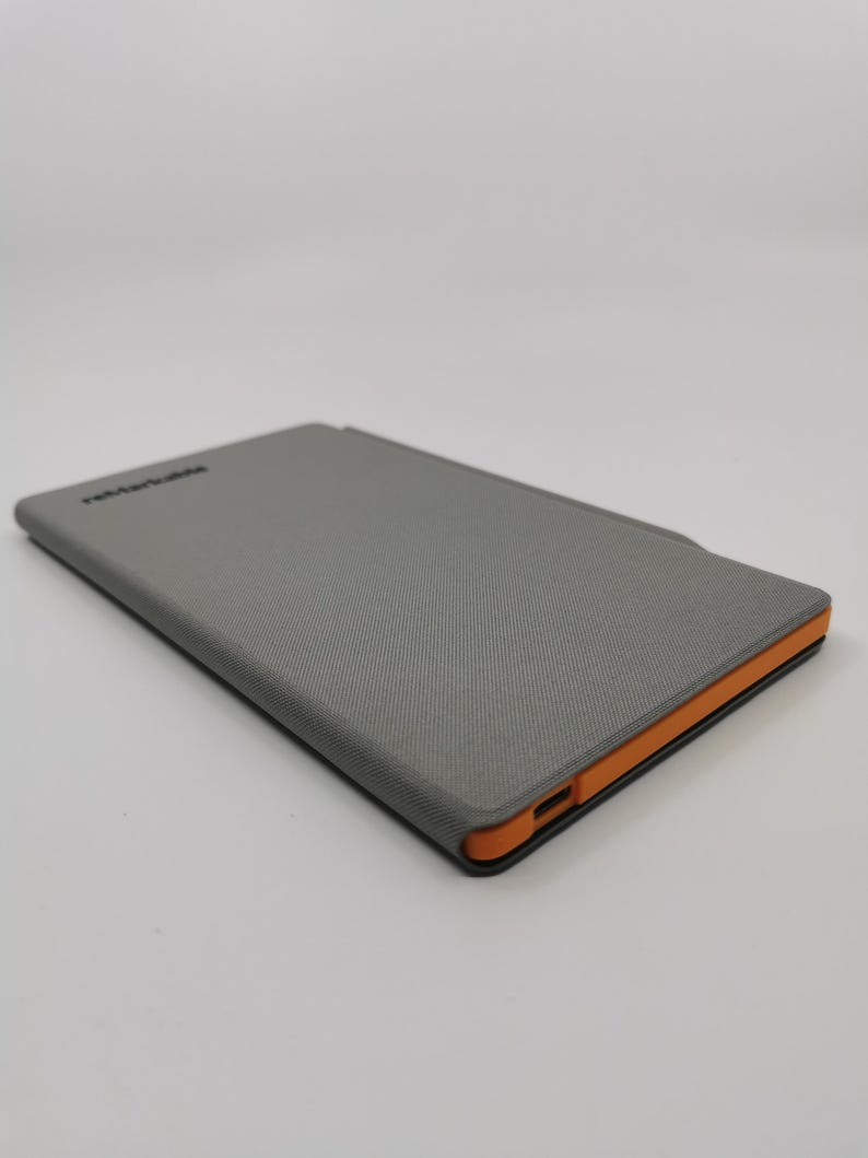 May include: A gray tablet case with an orange border. The case has a textured surface and the word "reMarkable" printed on the top. The case is rectangular and appears to be closed.