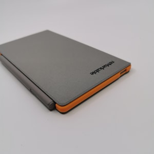 May include: A gray tablet with an orange border and a stylus. The tablet has the word "remarkable" printed on the top right corner. The tablet is closed and appears to be made of a textured material.