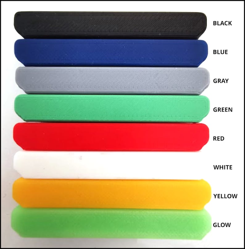 May include: A stack of rectangular, solid objects in various colors: black, blue, gray, green, red, white, yellow, and glow-in-the-dark green. Each object has a rounded edge and a textured surface. The colors are labeled with corresponding text.