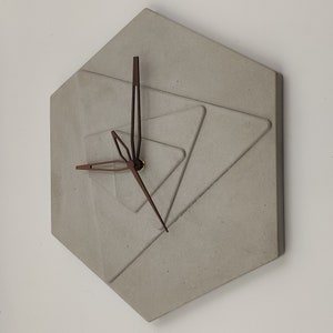 May include: A grey concrete hexagon clock with brown hands and a geometric design. The clock is mounted on a white wall.