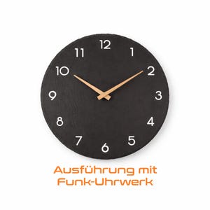 Könnte beinhalten: Eine runde schwarze Uhr mit weißen Ziffern und hellbraunen Zeigern. Das Zifferblatt hat eine strukturierte Oberfläche. Der Text "Ausführung mit Funk-Uhrwerk" ist unten aufgedruckt.