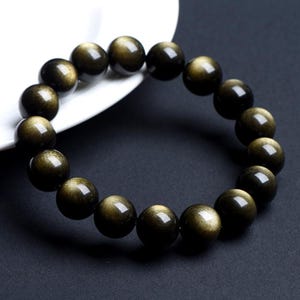 K&ouml;nnte beinhalten: Ein schwarzes Armband mit goldenen Sprenkeln. Die Perlen sind rund und glatt.