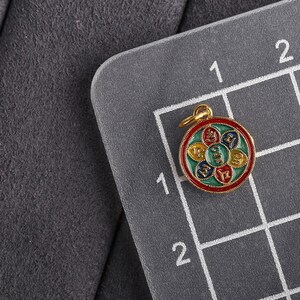 Puede incluir: Un colgante de color dorado con un dise&ntilde;o redondo y multicolor. El colgante presenta un dise&ntilde;o circular con seis secciones, cada una de un color diferente: rojo, verde, amarillo, azul y blanco. El centro del colgante tiene un s&iacute;mbolo dorado.