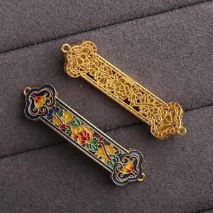 May include: Two gold-colored metal bookmarks with intricate floral designs. One bookmark features blue enamel with red and yellow accents, while the other bookmark is gold with a more detailed floral pattern.