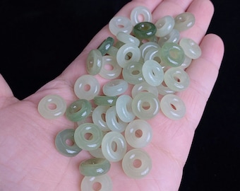 May include: A collection of jade donut beads in varying shades of green and off-white. The beads are round with a hole in the center, and are smooth and polished. The beads are a natural stone material.
