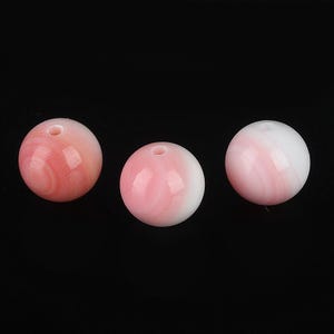 May include: Three round beads with a hole through the center. The beads are a mix of pink and white, with a swirled pattern. The beads are likely for jewelry making.
