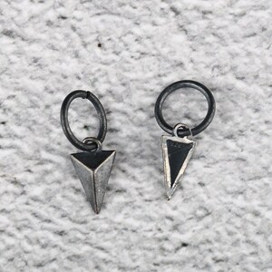 Pode incluir: Um par de brincos de prata com pingentes triangulares pretos pendurados em pequenos aros.