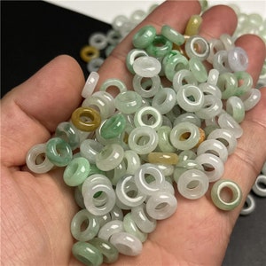 May include: A collection of green and white jade ring beads. The beads are smooth and polished, and they have a variety of shades of green.