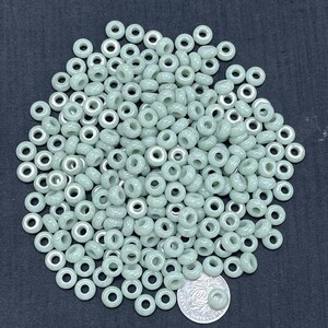 May include: A large pile of light green donut-shaped beads with a silver-colored hole in the center. The beads are approximately 6mm in diameter.