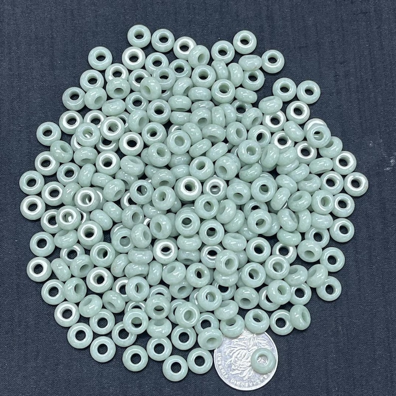 May include: A large pile of light green donut-shaped beads with a silver-colored hole in the center. The beads are approximately 6mm in diameter.