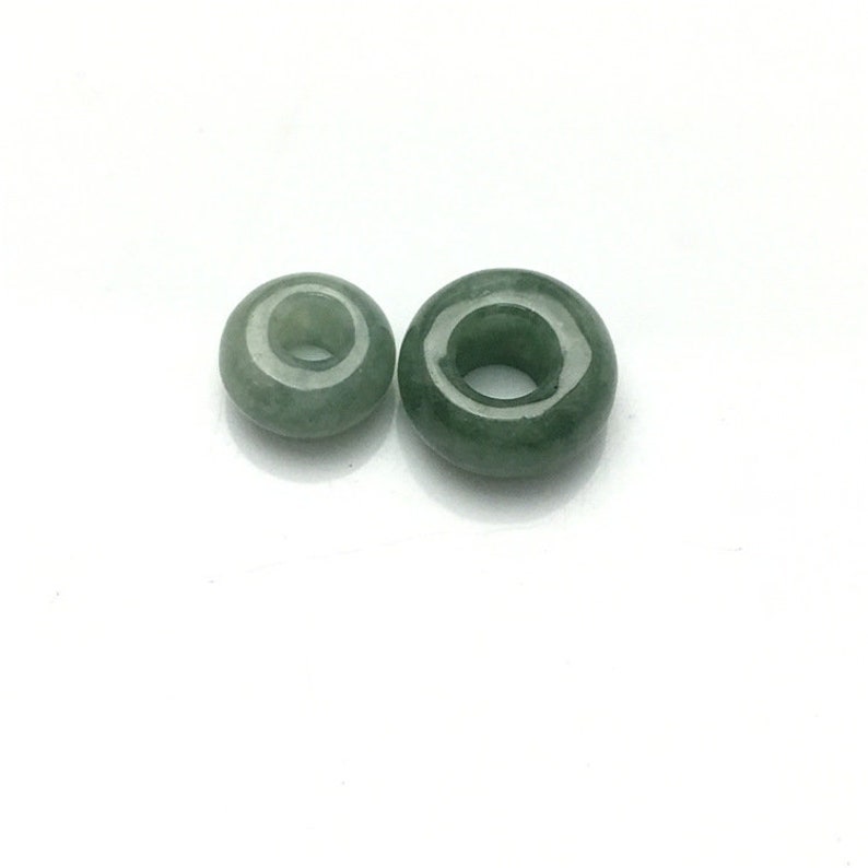 May include: Two green jade donut beads with a hole in the center. The beads are different sizes.