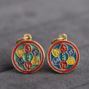 Puede incluir: Dos colgantes de oro con un dise&ntilde;o de esmalte rojo, azul, verde y amarillo. Cada colgante presenta un dise&ntilde;o circular con cinco p&eacute;talos y un s&iacute;mbolo en cada p&eacute;talo. Los s&iacute;mbolos son de color dorado.