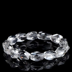 May include: A clear quartz crystal bracelet with faceted, irregular beads. The beads are strung together, forming a circular shape. The bracelet is displayed against a black background, highlighting its transparency and reflective qualities. The bracelet is a piece of jewellery.