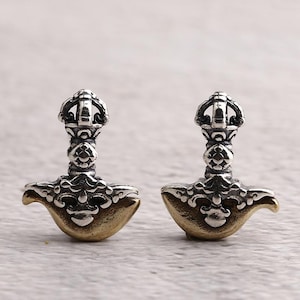 Può includere: Un paio di orecchini in metallo argentato e dorato. Ogni orecchino presenta un design dettagliato con una parte superiore decorativa e una forma curva a martello. Gli orecchini sono esposti su uno sfondo neutro.