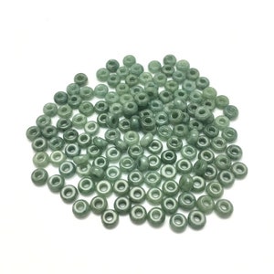 May include: A large pile of light green jade donut beads. The beads are smooth and polished, and they have a slightly translucent appearance.