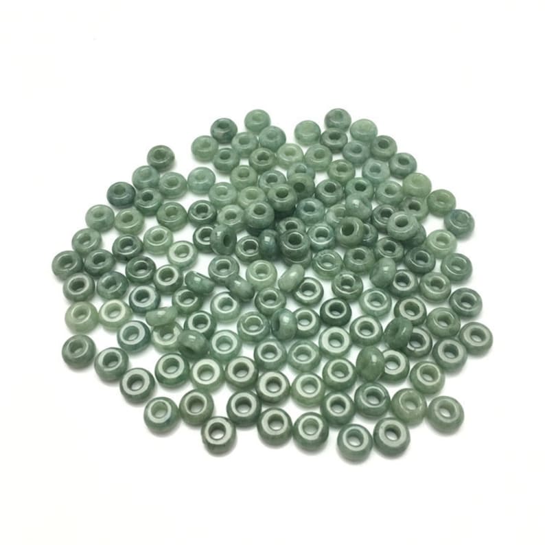 May include: A large pile of light green jade donut beads. The beads are smooth and polished, and they have a slightly translucent appearance.