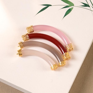 May include: Four different colored semi-circular bangle bracelets with gold filigree end caps. The bracelets are pink, red, gray, and white.