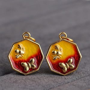 May include: Two gold-colored octagonal pendants with red and yellow enamel. Each pendant features a stylized butterfly and bee design.