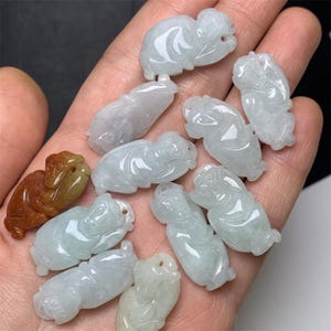 May include: A collection of jade pendants in various shades of green, each carved in the shape of a sleeping Buddha. The pendants are smooth and polished, with intricate details.