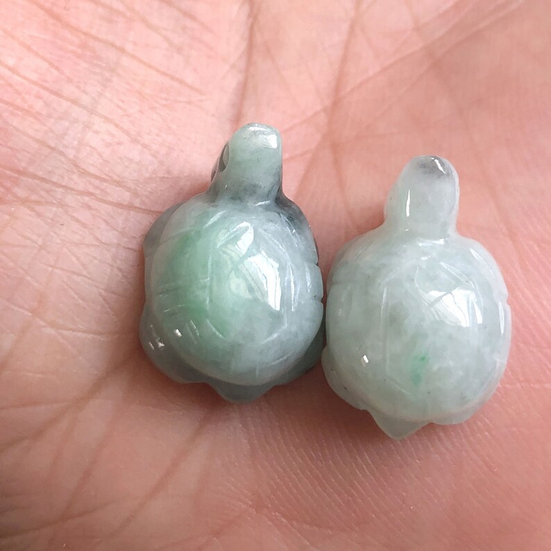 May include: Two jade green turtle charms, one slightly larger than the other, with detailed carvings of the turtle shell. The charms are smooth and polished.
