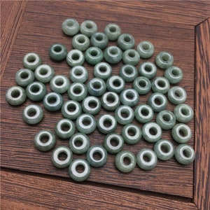 May include: A collection of light green jade beads with a hole in the center of each bead. The beads are arranged in a random pattern on a wooden surface.