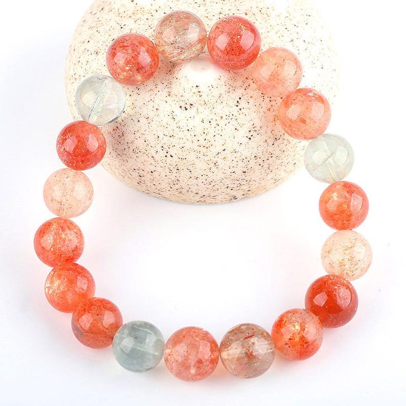 Op de afbeelding: Een armband gemaakt van oranje, witte en groene sunstone kralen. De kralen zijn rond en hebben een doorschijnende uitstraling.