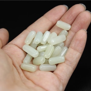 May include: A collection of smooth, off-white, cylindrical beads. The beads are made of a translucent material, possibly jade or ceramic.