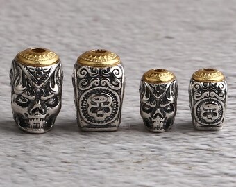 Puede incluir: Cuatro cuentas plateadas con forma de calavera y tapas doradas. Las cuentas presentan caras de calavera detalladas y patrones decorativos. Las cuentas cilíndricas varían ligeramente de tamaño.