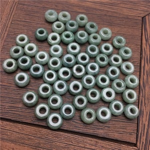 May include: A collection of 50 light green jade beads with a hole in the center. The beads are round and smooth.