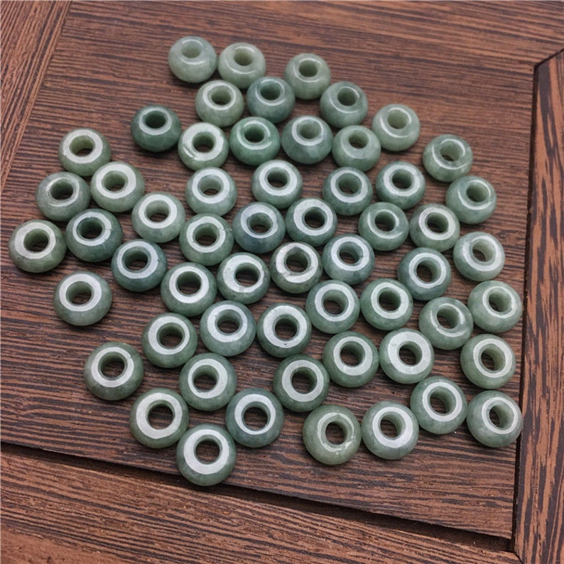 May include: A collection of 50 light green jade beads with a hole in the center. The beads are round and smooth.