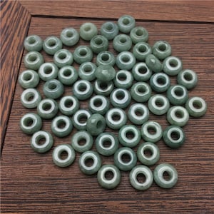 May include: A collection of green jade beads with a hole in the center. The beads are arranged in a random pattern on a wooden surface.