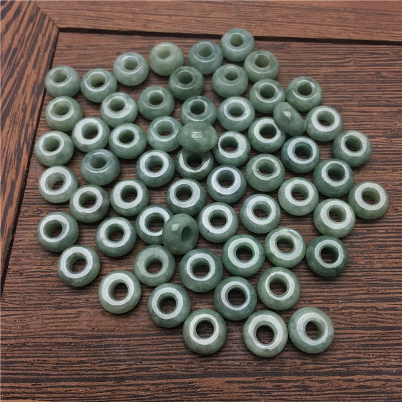 May include: A collection of green jade beads with a hole in the center. The beads are arranged in a random pattern on a wooden surface.
