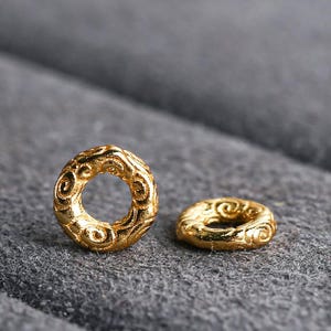 Può includere: Due anelli in metallo color oro con intricati disegni a spirale. Gli anelli hanno un diametro di circa 1 cm.