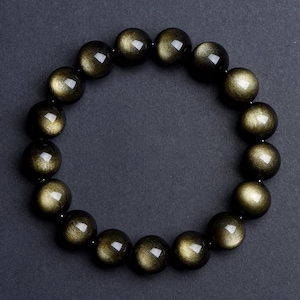 May include: A black bracelet with gold flecks, made of round beads. The bracelet is on a dark gray background.