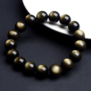 K&ouml;nnte beinhalten: Ein schwarzes Armband mit goldenen Sprenkeln. Die Perlen sind rund und glatt.
