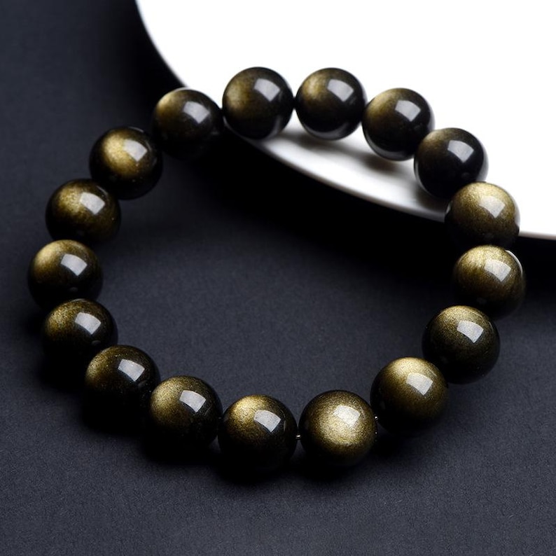 K&ouml;nnte beinhalten: Ein schwarzes Armband mit goldenen Sprenkeln. Die Perlen sind rund und glatt.