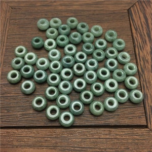 May include: A collection of green jade beads with a hole in the center. The beads are smooth and polished, and they are arranged in a random pattern.