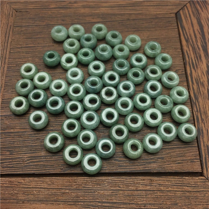 May include: A collection of green jade beads with a hole in the center. The beads are smooth and polished, and they are arranged in a random pattern.